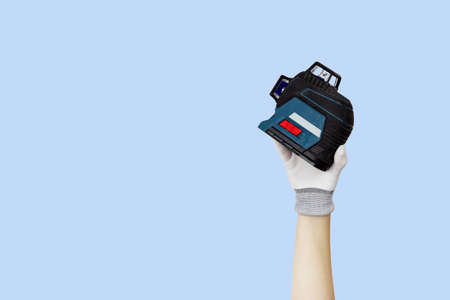 Gloved hands holding laser level construction tools. Work tools on blue backgroundの写真素材