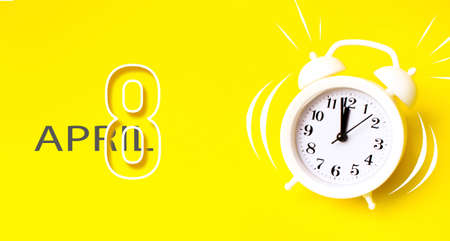 April 8th. Day 8 of month, Calendar date. White alarm clock with calendar day on yellow background. Minimalistic concept of time, deadline, time to work, morning. Spring month, day of the year conceptの写真素材