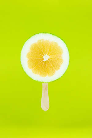 Grapefruit sweetie icecream with wood stick on light green background. Creative summe fruity popsicle sticksの写真素材