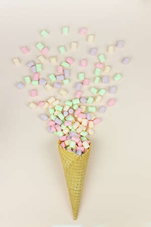 Yellow waffle cone with green, pink and yellow marshmallows on pastel background