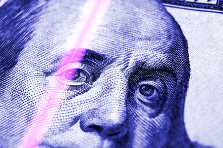 Checking dollar banknotes in a UV light. Counterfeit money concept. Benjamin Franklin's eyes from a...