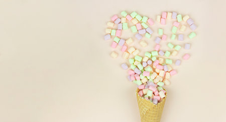 Layout with waffle cone cornet and colored marshmallows in form heart on pastel background