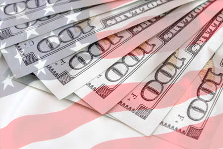 US dollar background with american flag background. Economy, savings and the US dollar. Several 100 US money notes spread out in fan shapeの写真素材