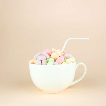 Beautiful variety of marshmallows looks like macaroons in porcelain white coffee cup mug with straw on pastel pink background. Brignt macarons for sweet breakの写真素材