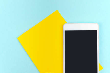 Yellow a piece of paper with empty screen mobile phone on blue background