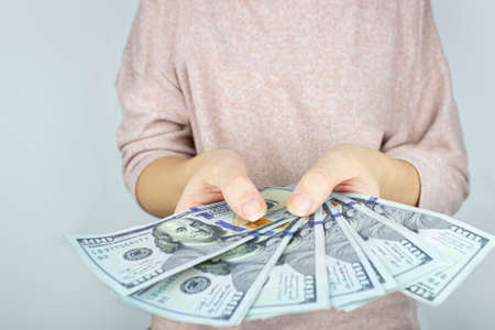 Female hand holding stack of 100 dollar bills fanned out on gray background. Money Financial and Payment Conceptの写真素材