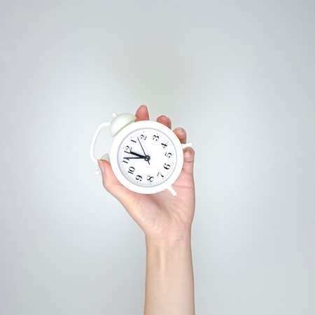 Hand holding alarm clock on light background. Schedule concept with empty copy spaceの写真素材