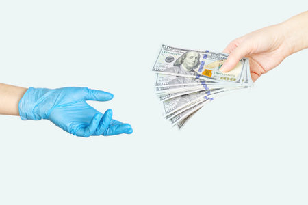 treatment payment concept. Transfer of money from hand to another hand in blue medical glove. Bribe to the doctor. Paid medicine conceptの写真素材