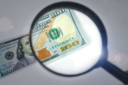 Zoom to money. Magnifying Glass - 100 US Dollars. Concept on the theme of checking money for authenticityの写真素材