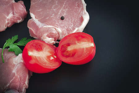 Sliced raw pork meat for grilling on dark background with ingredients for cookingの写真素材