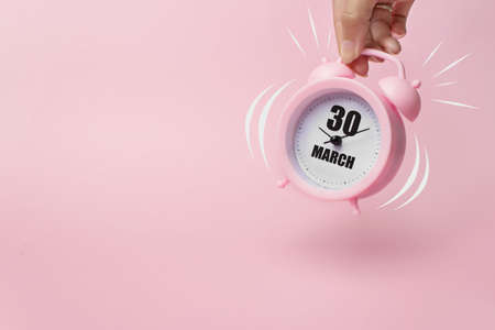 March 30th. Day 30 of month, Calendar date. The morning alarm clock jumping up from the bell with calendar date on a pink background. Spring month, day of the year conceptの写真素材