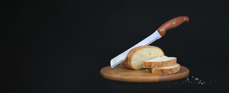 Wooden cutting board with sliced white bread and knife on black backgroundの写真素材