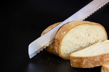 Knife slicing freshly baked loaf of bread. Close-up metal kitchen knife cuts bread on cutting board