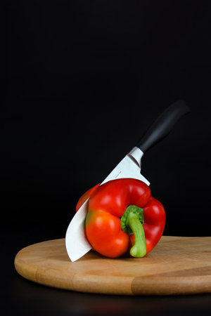 Closeup of Sharp Knife cutting red pepper on wooden board.