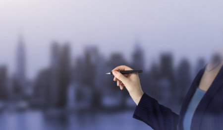 Female hand writing with a pen on city background, black pen in hand. Closeup of hand holding a black marker about to write somethingの写真素材
