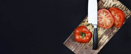 Wooden board with chopped tomatoes. The knife cuts a tomato in half. Fresh Cut Tomatoの写真素材