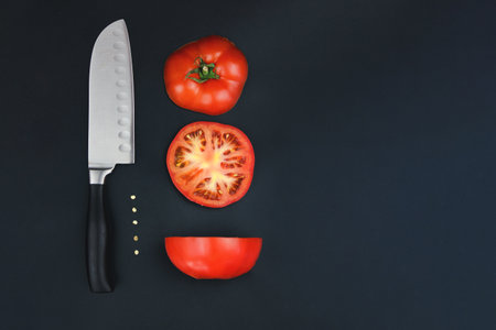 A tomato cut into two halves with a sharp knife. Circles of red tomatoes with knife on black background. Harvesting tomatoes. Concept for healthy nutrition. top view. copy spaceの写真素材