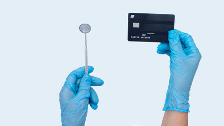 Female dentist hand holds dentist mirror and credit card. light background. Concept of Cost of...