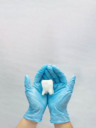 Woman hand holding white tooth on pastel blue background. Dentist stomatology medical conceptの写真素材