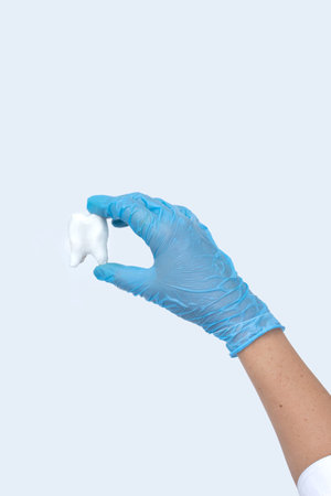 Woman hand holding white tooth on pastel blue background. Dentist stomatology medical concept
