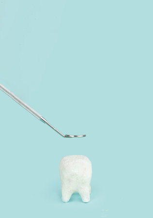 White ceramic tooth on blue background with dentist mouth mirror, copy space, close-upの写真素材