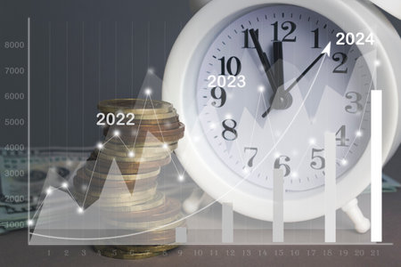 White alarmclock with Coins stack and stack of one hundred dollar bills with Financial charts...