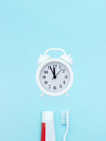 Closeup of a toothpaste, toothbrush and white alarmclock on blurred blue background. Teeth or dentures concept on blue background. Means to care for the oral cavityの写真素材