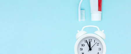 Closeup of a toothpaste, toothbrush and white alarmclock on blurred blue background. Teethcare,...