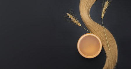 Blond long hair with cream jar and sprigs of ripe wheat. Healthy hair. Black background. Hair tools, beauty and hairdressing concept. Hair care, healthy.の写真素材
