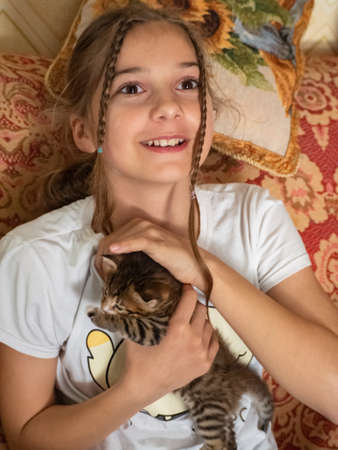 Happy girl with a kitten. A teenage girl smiling looks out the window and strokes a cute little kitten. real life. Joyful emotions on the child's face.の写真素材