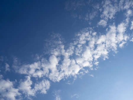 Blue sky with clouds. natural sky background. The upper left corner is dark blue, the lower right corner is light blue illuminated by the sun, in the center diagonally white fluffy clouds.の写真素材