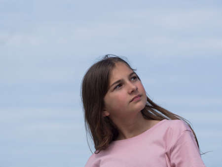 A beautiful, thoughtful girl looks up into the distance. Soft blue sky in the backgroundの写真素材