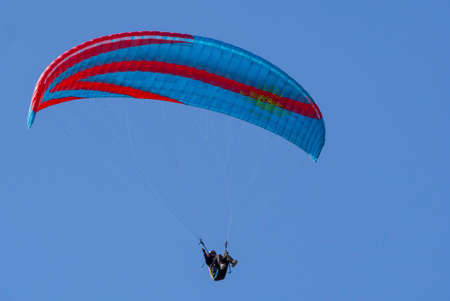 A paraglider flies by parachute in the blue sky. Paragliding on a sunny day. Wide-angle view of a paraglider flying high in the sky on a blue background. Russia Krasnodar Kamyshevatskaya 14.06.2021.の写真素材