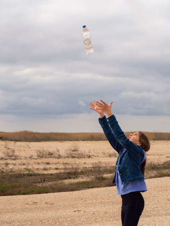 A girl with her head raised and her arms outstretched to the sky, a bottle falls from the sky, and...