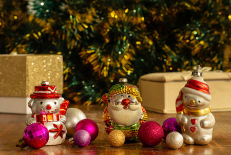 Christmas decorations-toys (snowmen, Santa Claus and balloons) lie on a wooden table. Boxes with gifts and green tinsel with yellow tips are visible on a defocused background.の写真素材