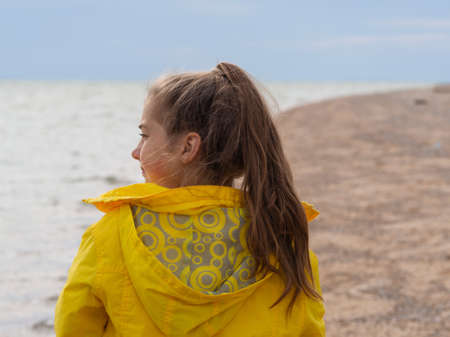 A beautiful teenage girl in a bright yellow jacket on a deserted beach near the sea. The girl looks into the distance. The sea and the beach are out of focus.の写真素材