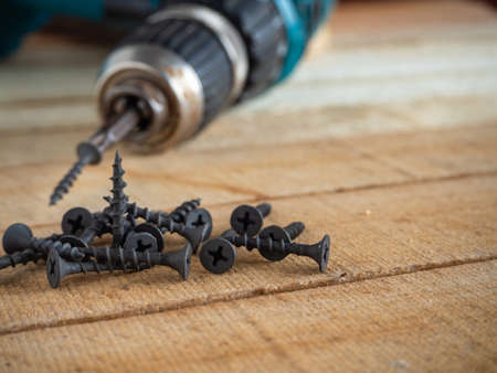 self-tapping screws on the background of a screwdriver. Lots of screws and a screwdriver on wooden...
