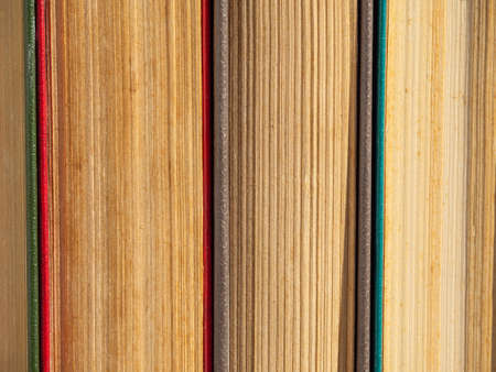 Abstract textured background of pages of closed hardcover books. Old battered books with yellowed pages from time close-up. Close-up of old books standing side by side on a bookshelf.の写真素材