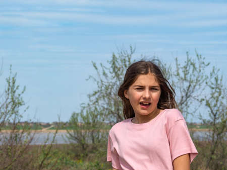 Sneezing teenage girl in early spring in nature. Portrait of a beautiful girl with signs of a spring exacerbation of allergy to flowering. A girl in a pink T-shirt is standing outdoors.の写真素材
