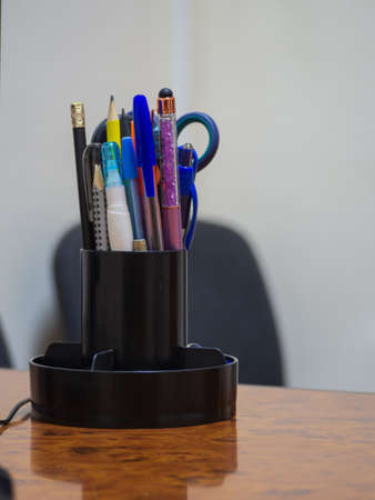 Stationery in the organizer on the desktop. Close-up of an organizer with used pens and pencils on a wooden desk in the office. office supplies. Pens in a cup on the conference table.の写真素材