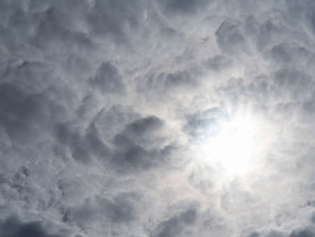 Solid cumulus clouds and pale sun breaking through them, textured cloud background. The Sky And Gray...