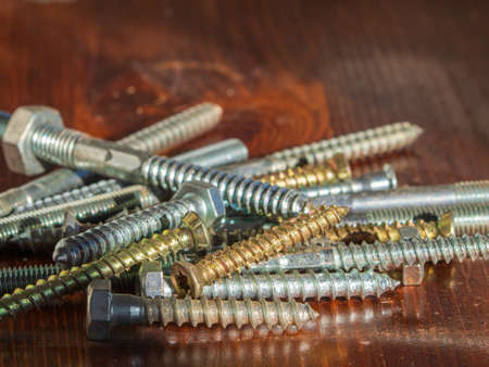 Various mounting bolts on the wooden surface. Bright bolts and screws on a wooden background close-up. Close-up of various screws and boltsの写真素材