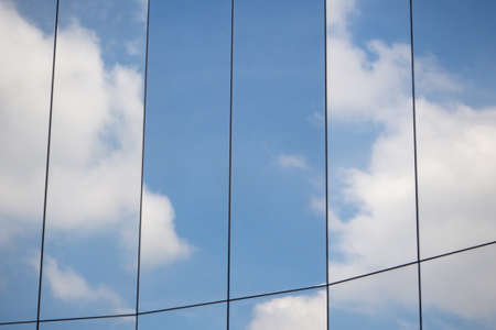 Reflection of clouds and blue sky on the surface of the glass wall of a modern building in a vertical frameの写真素材