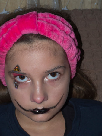 A close-up portrait of a beautiful girl with colored face art on her face. A teenage girl with makeup on her face looks at the camera from under her browsの写真素材