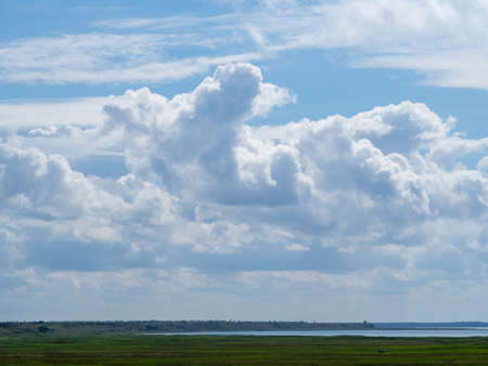 beautiful cloud landscape. White clouds in a blue sky over the bay and a green meadowの写真素材
