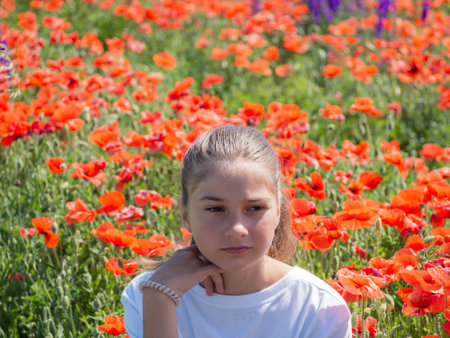 A girl with blonde hair is resting on a field with red poppies. A teenage girl in close-up in the rays of the sun on a field with poppies. An atmospheric authentic momentの写真素材
