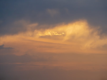 A dim sunset sky with clouds and dramatic light. Warm colors, space to copy. Picturesque storm clouds illuminated by the last rays of sunsetの写真素材