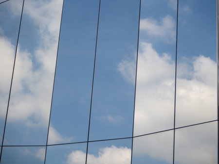 The blue sky and white clouds are reflected on the polished surface of the modern buildingの写真素材