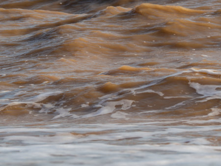 Texture of the water surface with turbid yellow-brown waves close-upの写真素材
