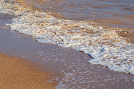 Waves with foam on a sunny summer day on a sandy beach. nature background. Beach scene with sea waves and sandの写真素材